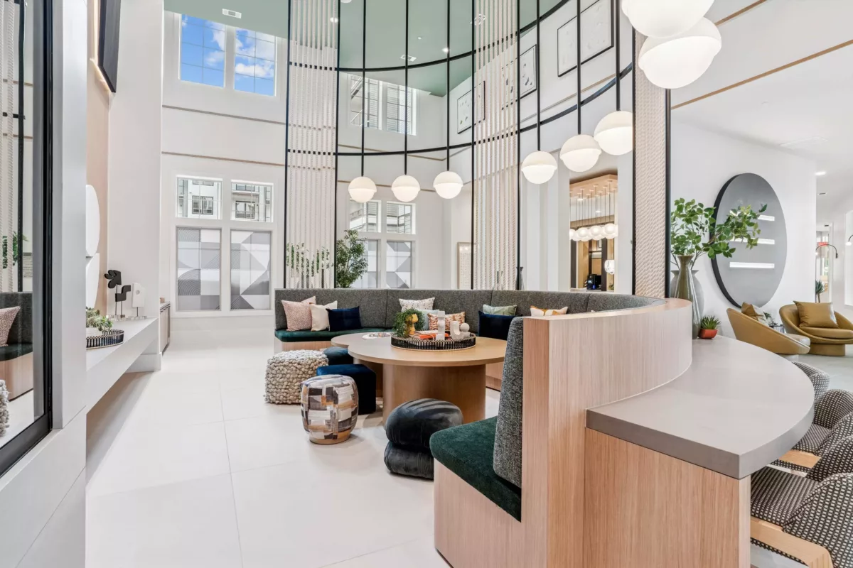Clubroom with curved seating, round tables, pendant lighting, and double-height windows.
