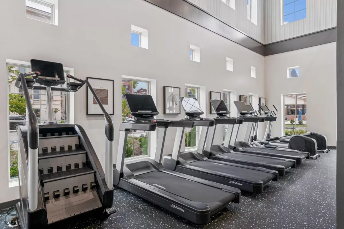 Fitness center with treadmills, stair climber, and elliptical machines in front of several windows.