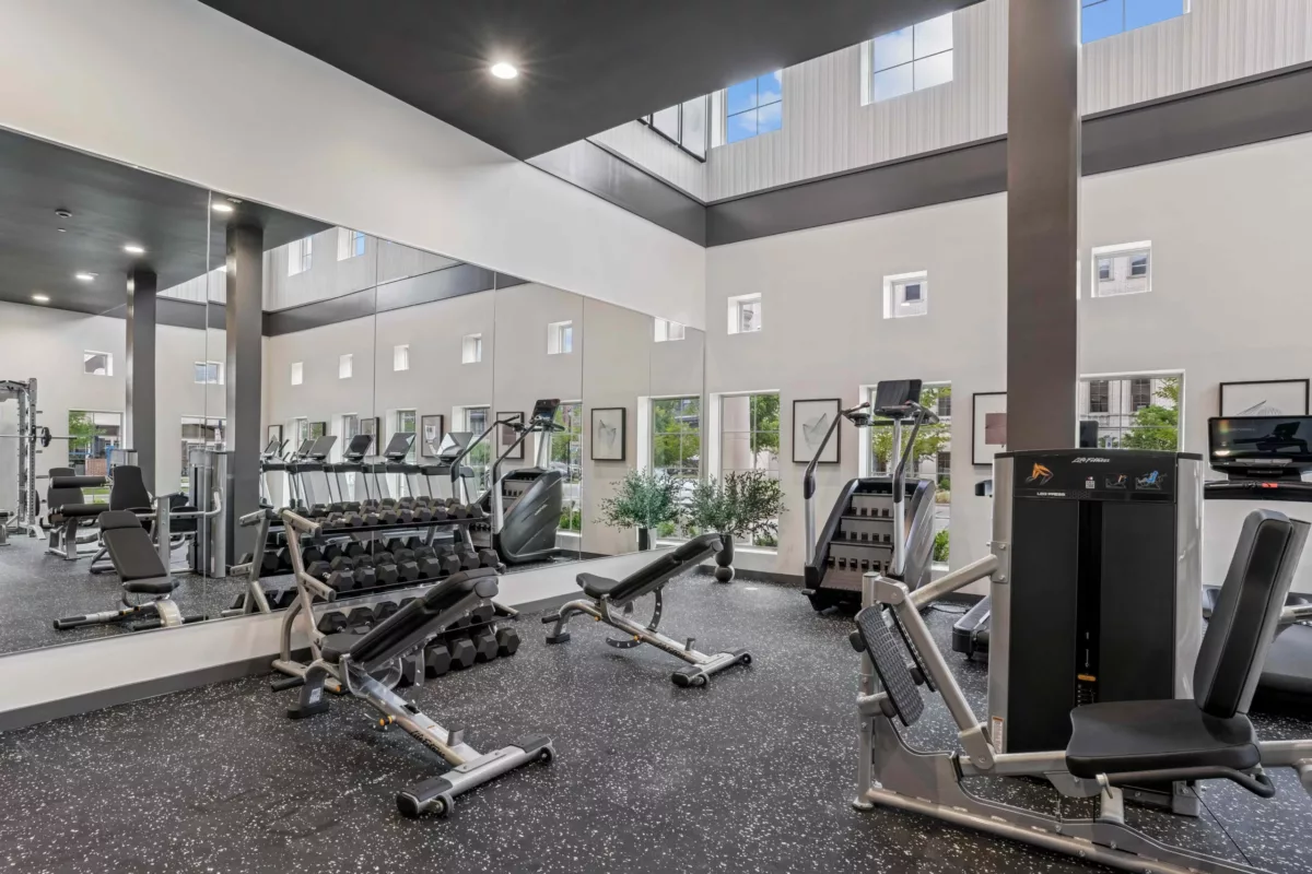 Fitness center with treadmills, weights, and weight machines and two stories of windows.