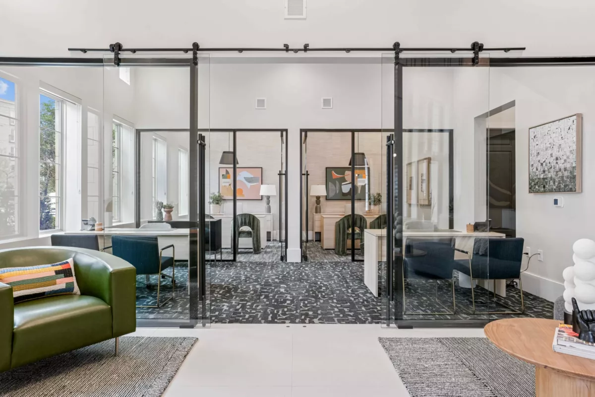Leasing lounge with glass-enclosed offices, desks, chairs, and modern decor.