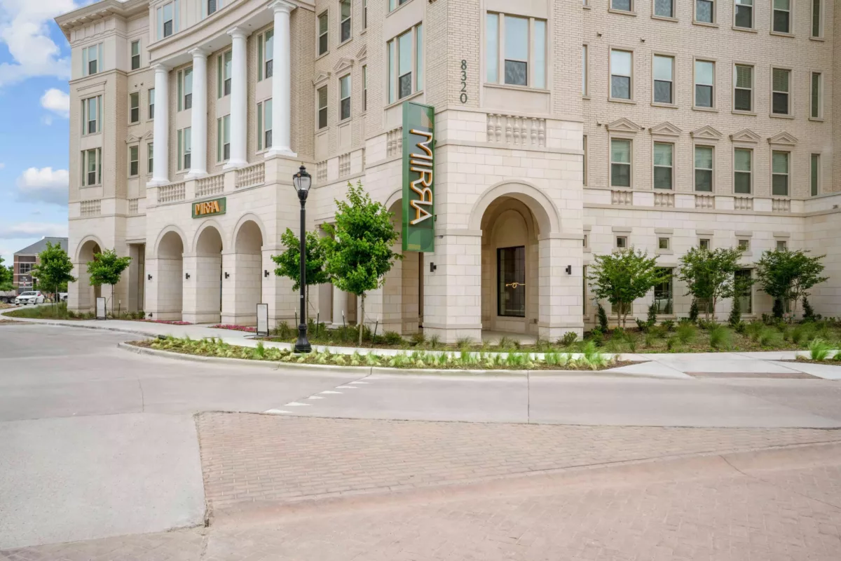Building exterior with arched entryway, columns, and brick facade with a vertical sign that says "Mirra".