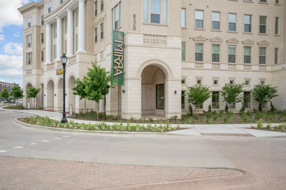 Exterior of a light brick building with arched entrances and white columns with a vertical sign that says "Mirra".