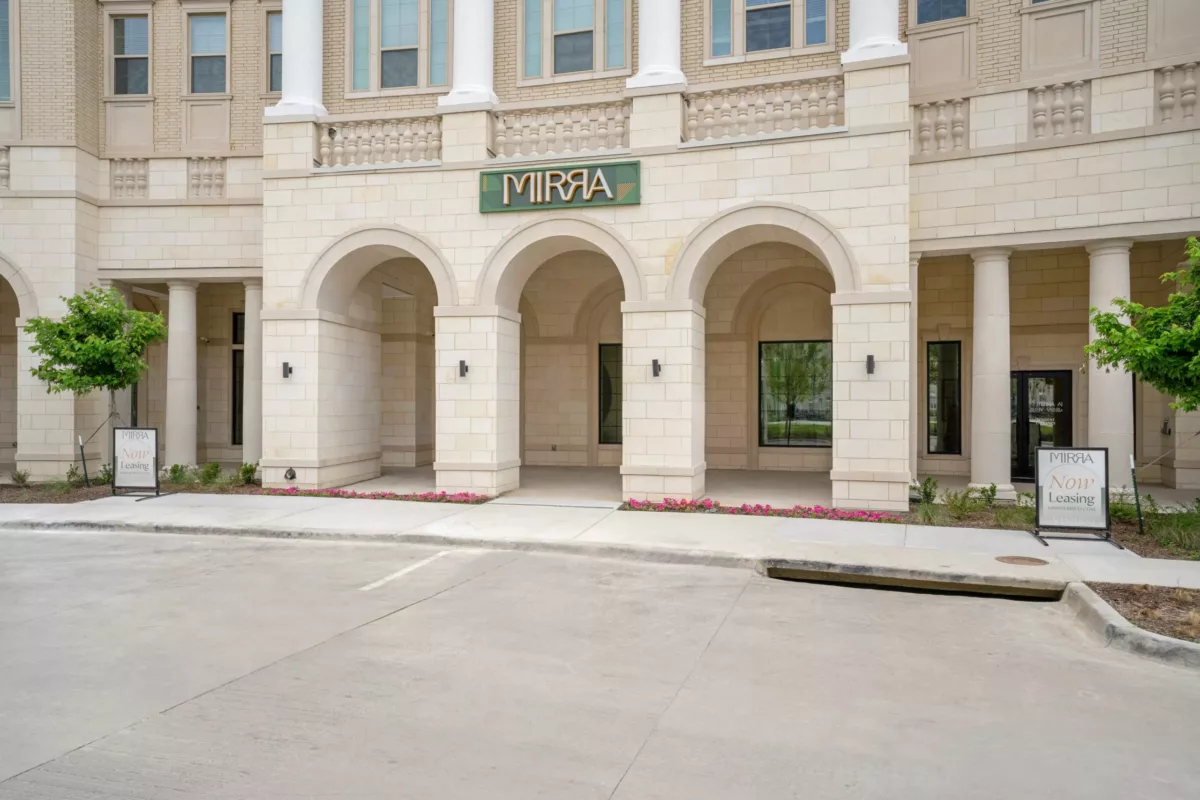 Building facade with arched entryway, columns, and stone detail with a sign that says "Mirra".