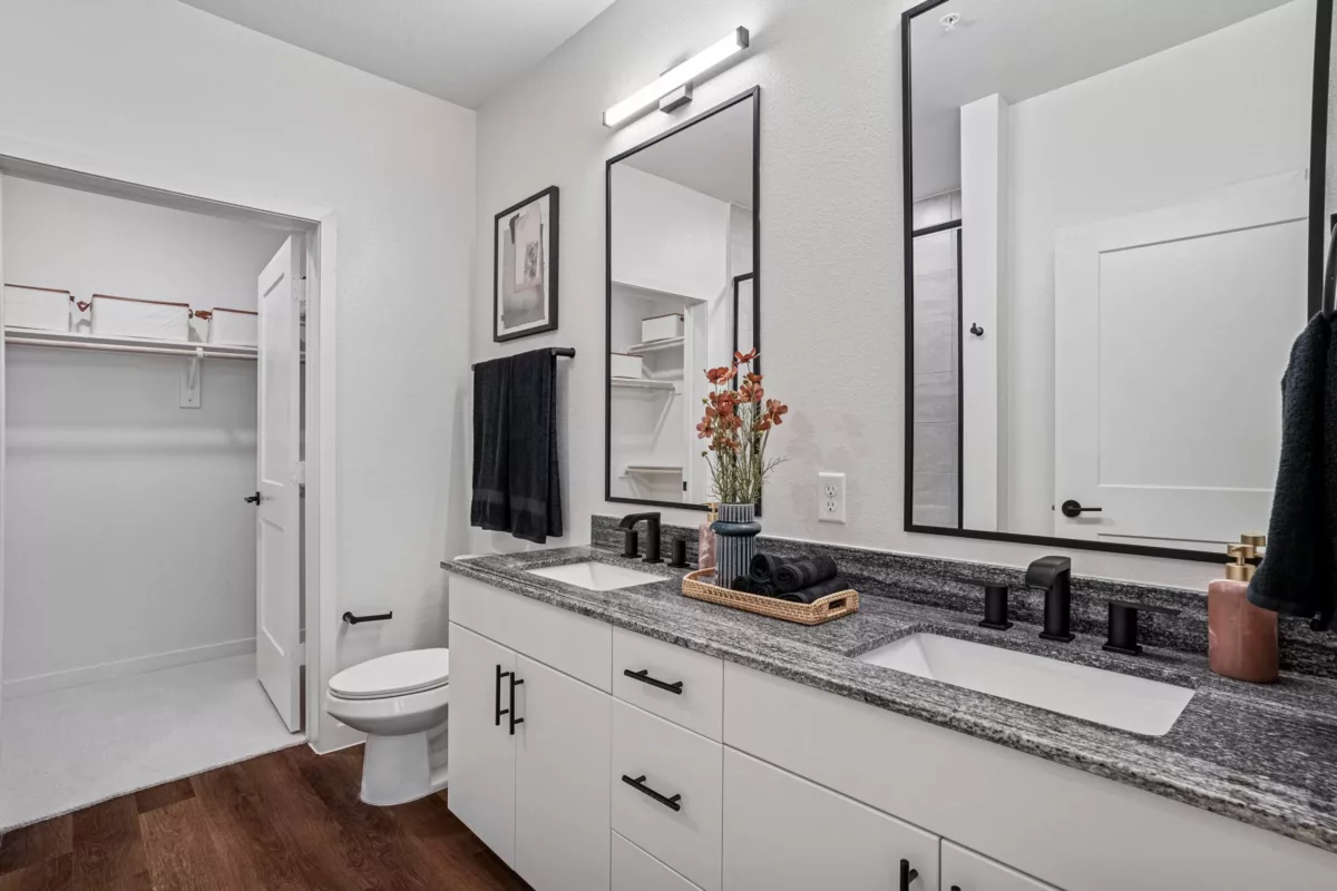 Bathroom with double vanity, granite countertop, black fixtures, and a door opened to a closet.