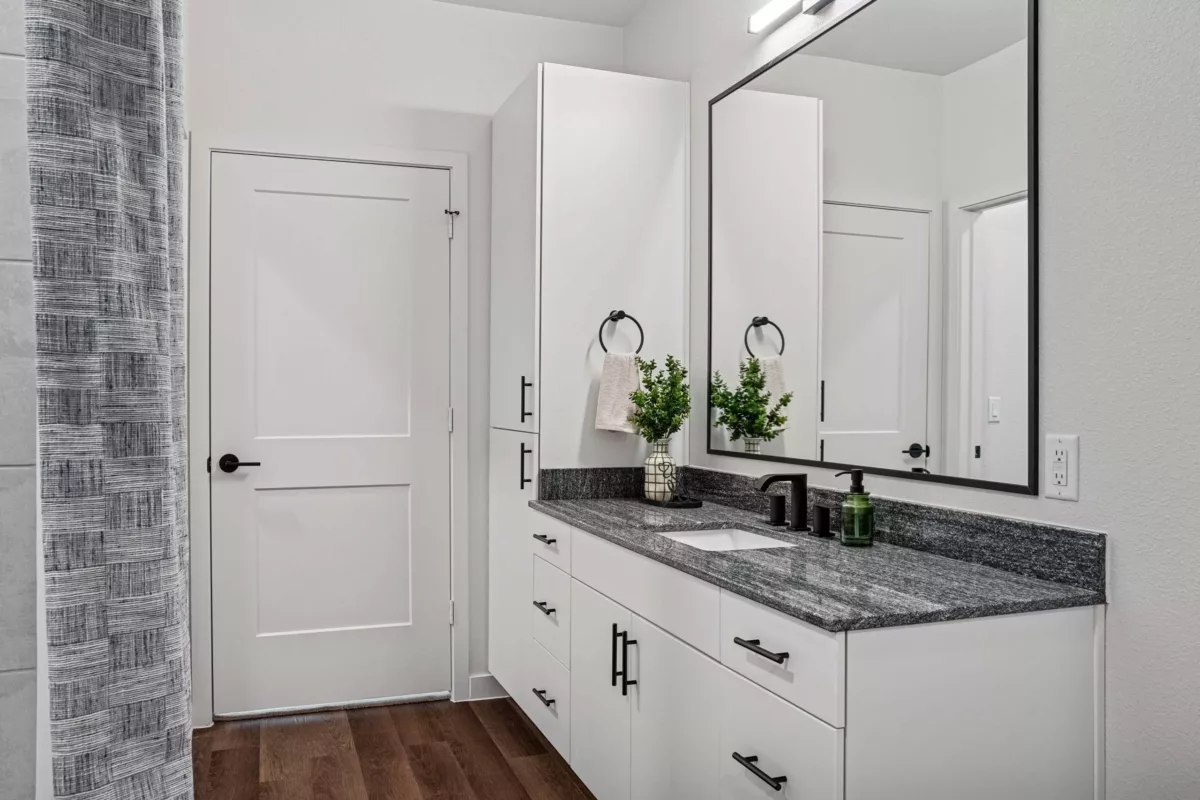 Modern bathroom with white vanity, granite countertop, black hardware, and framed mirror.