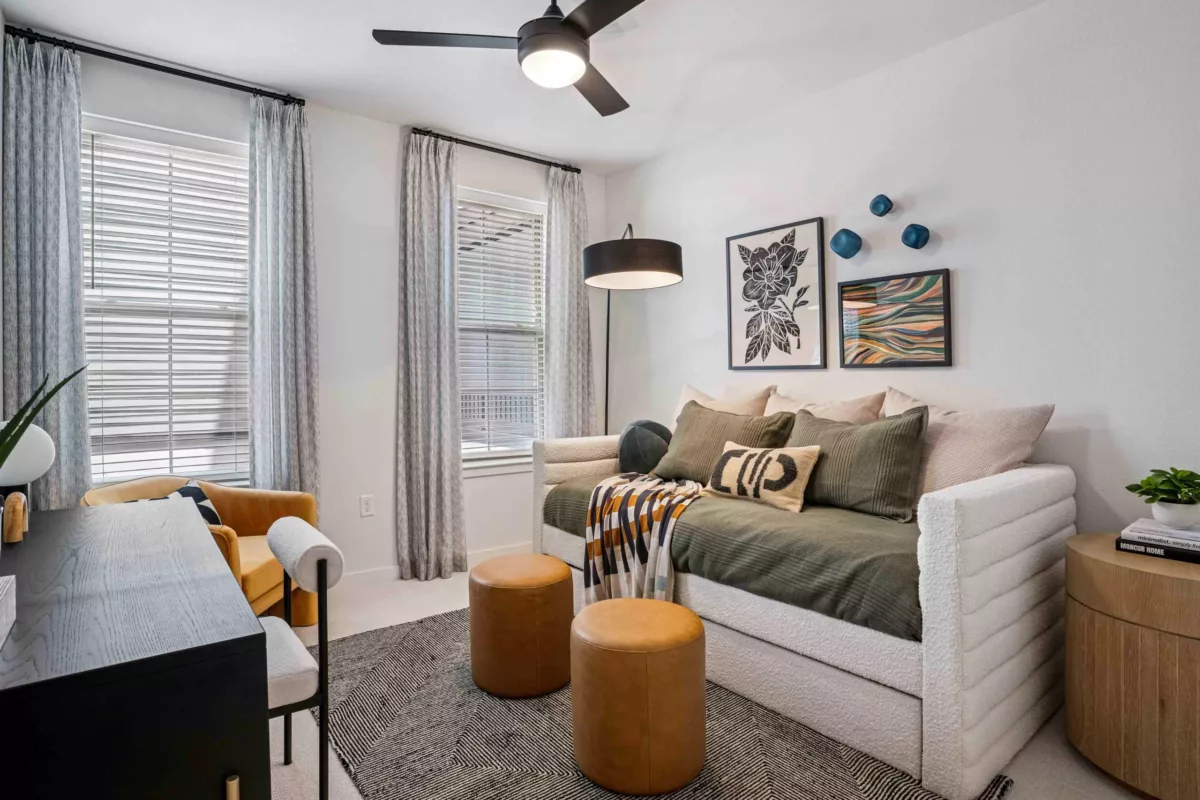 A bedroom with daybed, desk, chair, and leather ottomans on patterned rug.