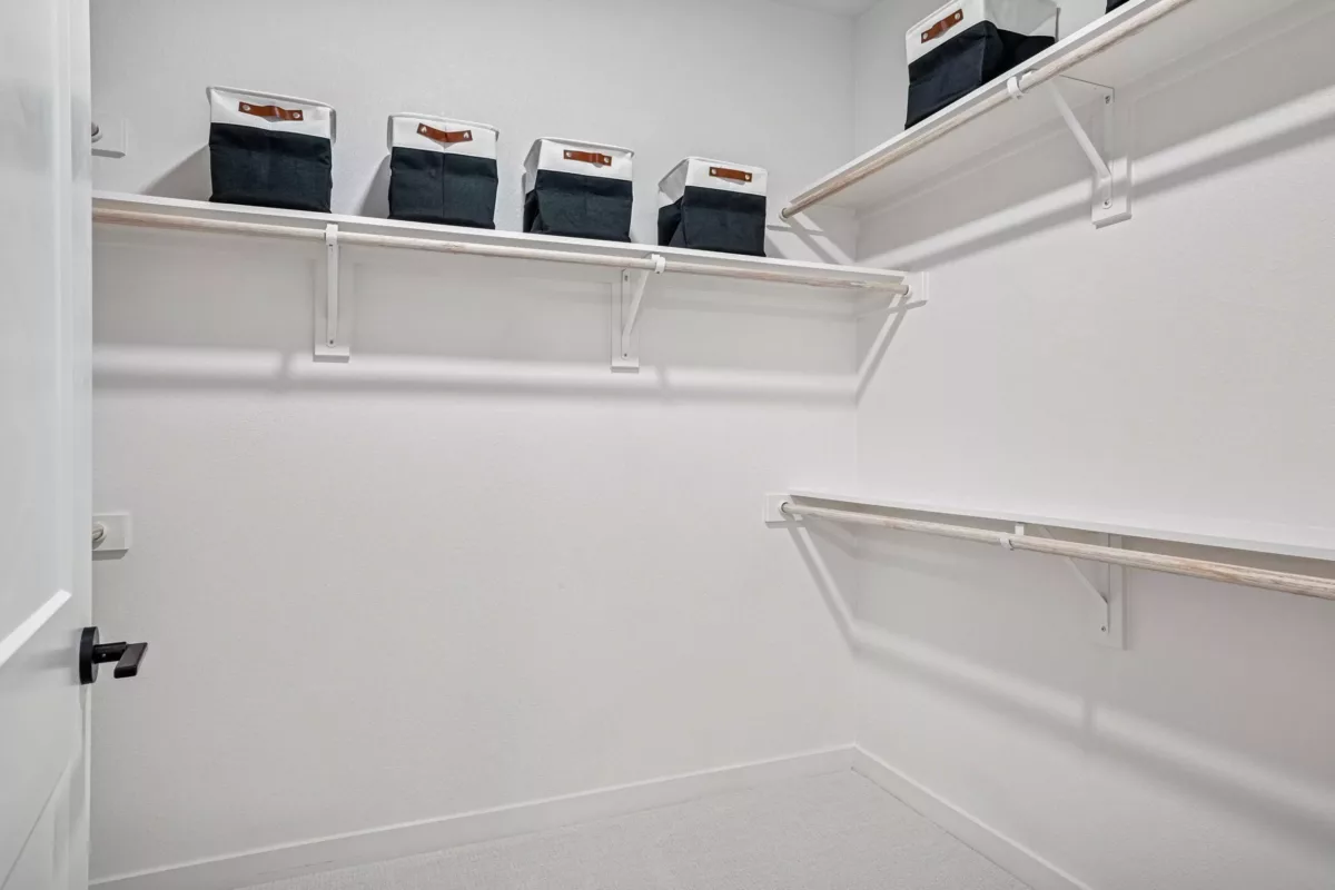 Oversized closet with white walls, carpet, shelving, and storage bins.