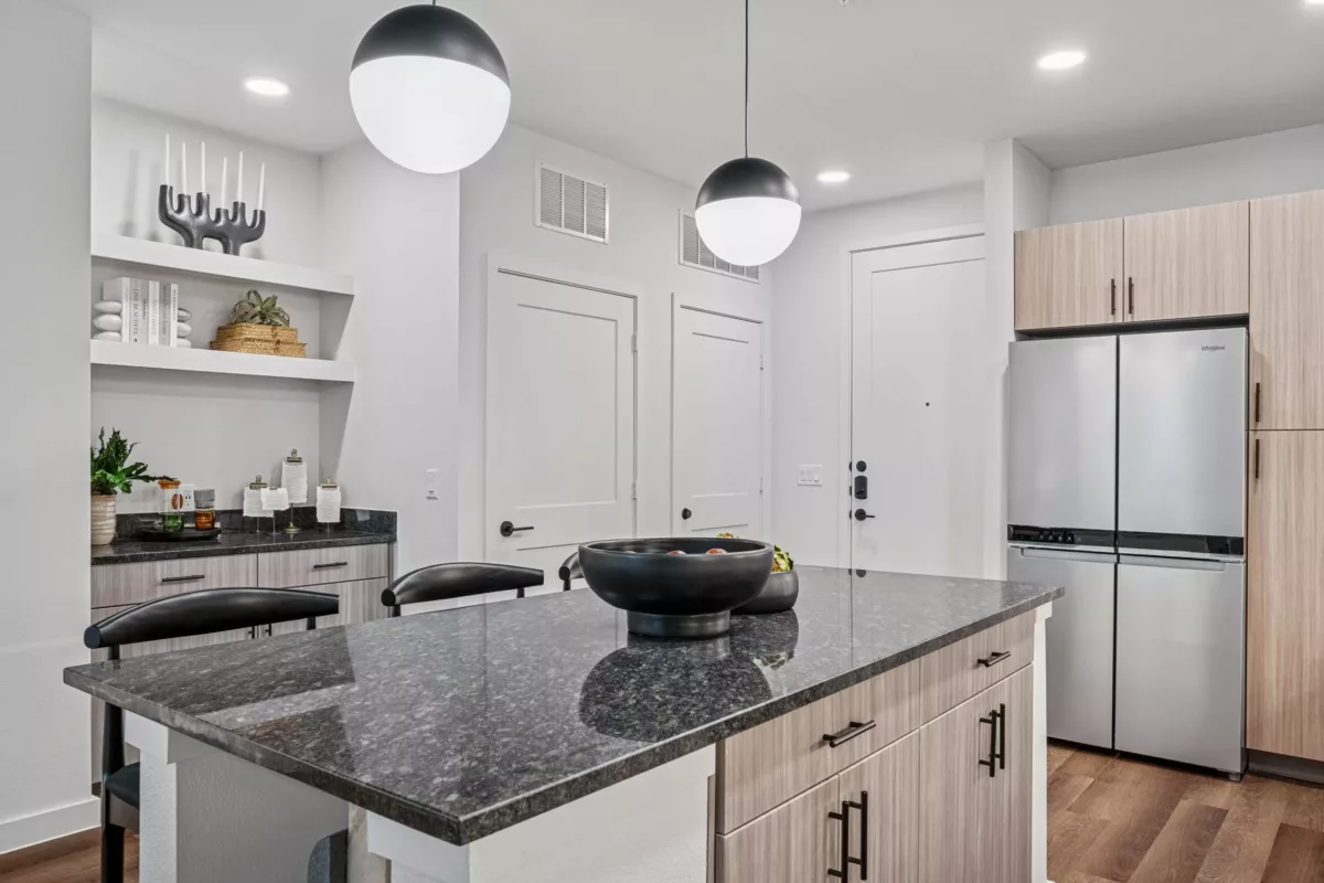 Kitchen with granite island, stainless steel refrigerator, and light wood cabinets.