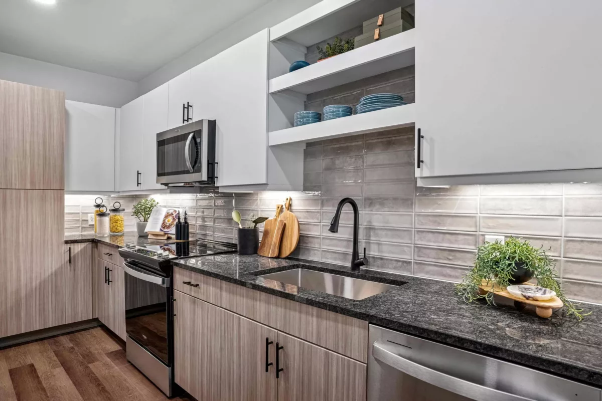 A modern kitchen with a stainless steel sink, black faucet, granite counters, and gray backsplash.