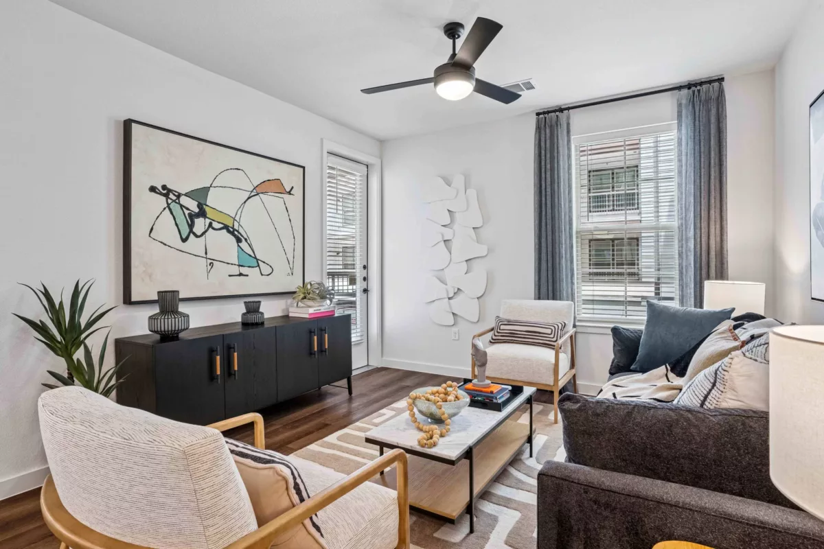 Living room with hardwood floors, sofa, chairs, modern wall art, and a ceiling fan.