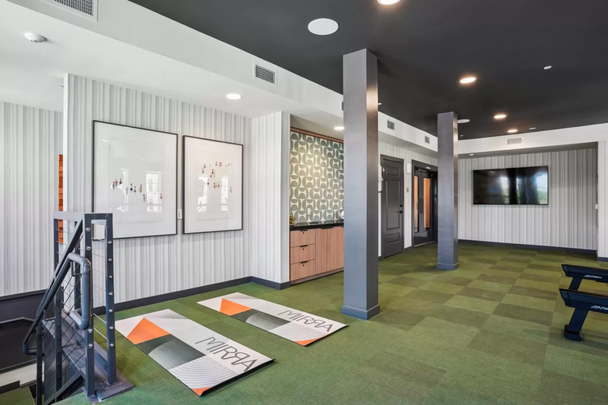 Fitness area with yoga mats, equipment, and mounted television on striped wallpaper.