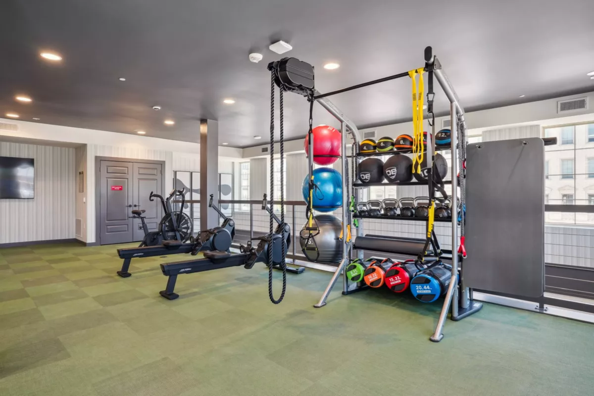 Fitness center with rowing machines, exercise bikes, and weight rack with medicine balls.