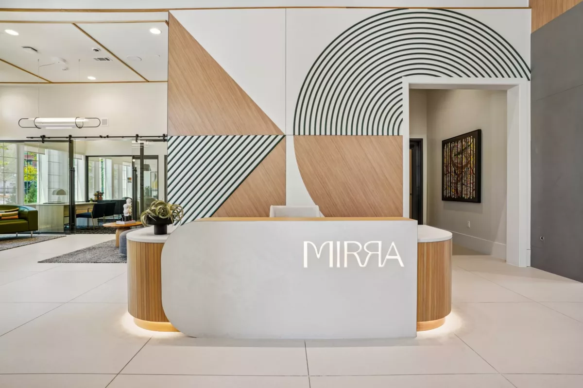 Grand lobby with reception desk, wood accents, and geometric wall design. Lounge seating available in front of leasing center.