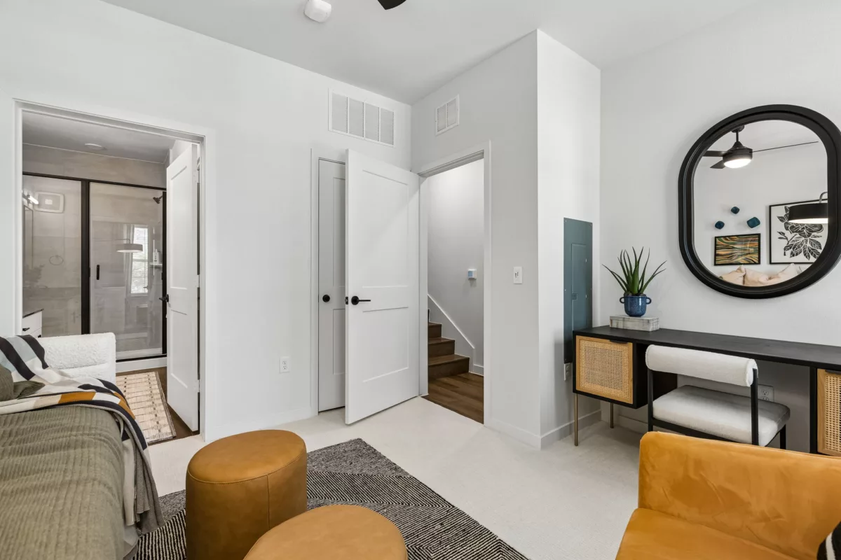 Bedroom with ottomans, desk vanity, open doors to hallway and bathroom with glass shower